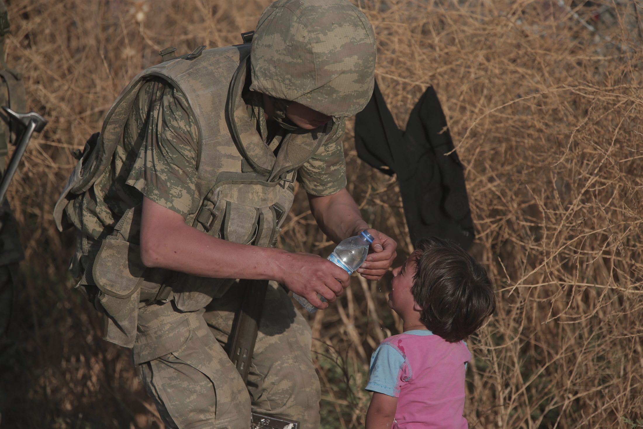 ایک ترک سپاہی پیاس سے بے حال ایک شامی بچی کو پانی پلاتے ہوئے۔ یہ بچی رواں سال جون میں سرحد عبور کرکے ترکی کے جنوب مشرقی صوبے شانلی عرفہ میں داخل ہونے والے ہزاروں شامی باشندوں میں سےایک تھی۔ 